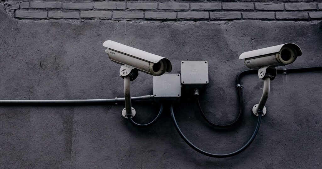 監視カメラと暗い影、企業を取り巻く政治的圧力のイメージ